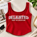 A red sleeveless crop top with white text reading 'DELIGHTED KEEP ON DISCIPLINE' laid flat on a beige fabric surface.